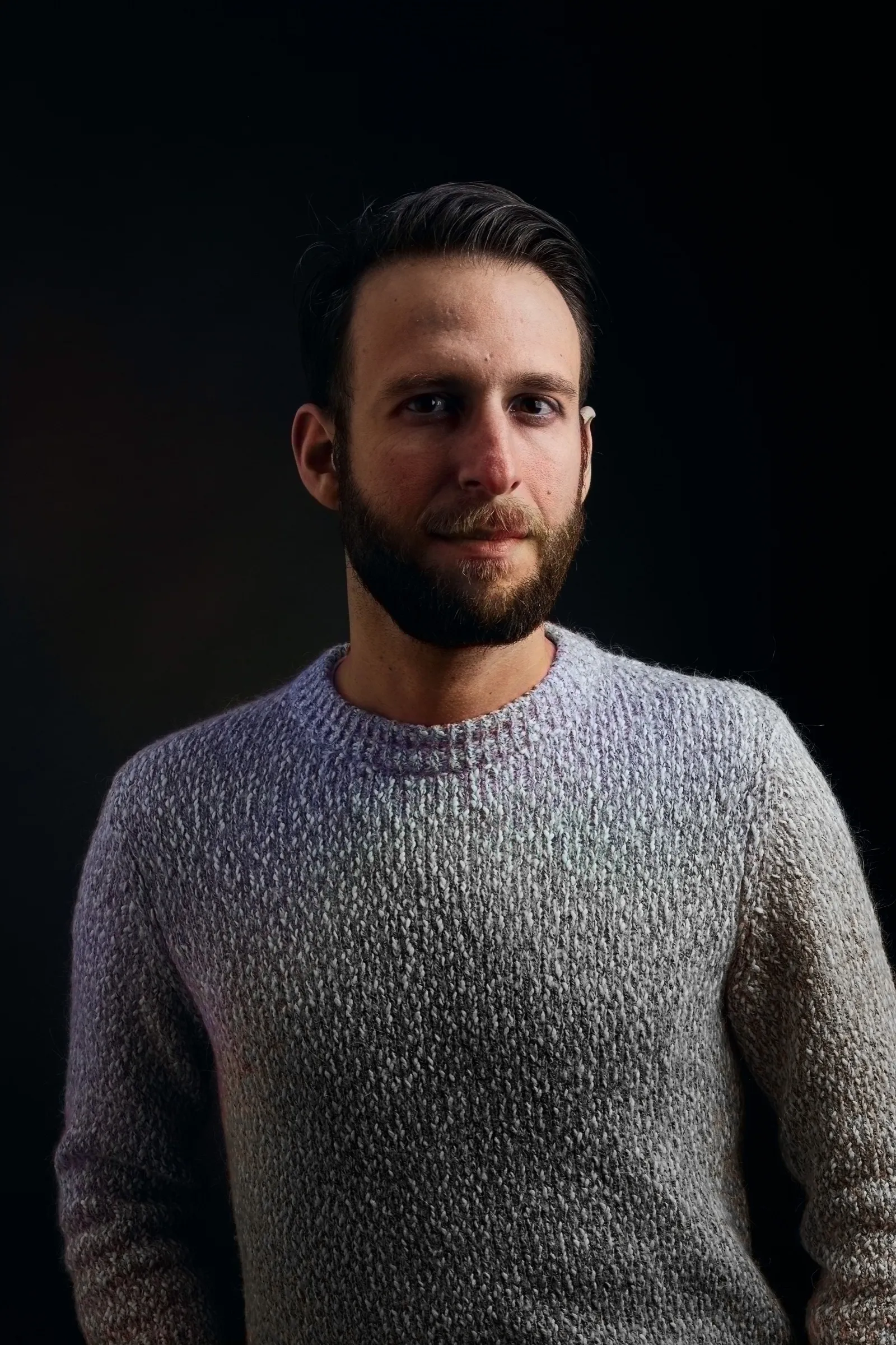Portrait of Adam in a grey knit sweater against a dark background